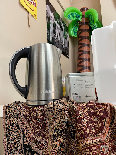 The Tea Club Table located in B207, with a box of tea, an electric kettle, and the inflatable palm tree hanging over.
